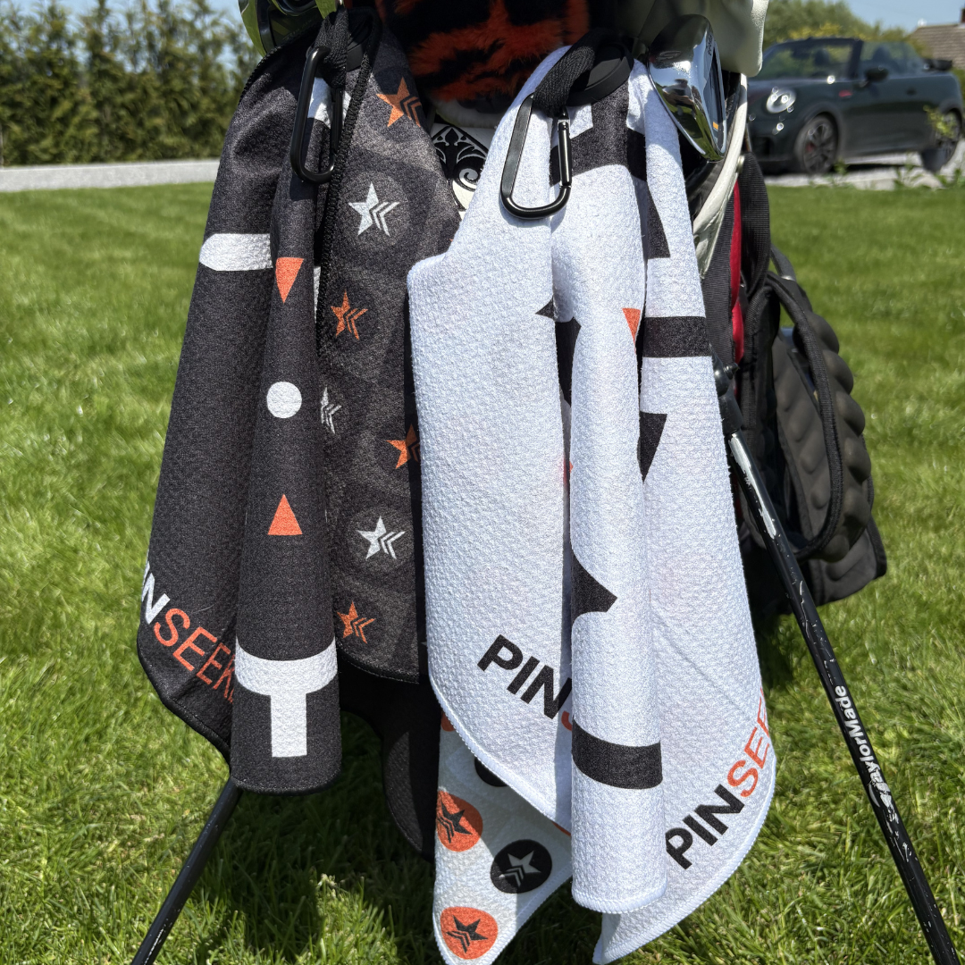 PINSEEKER golf towels in Blackout and Whiteout clipped to a golf bag on the course