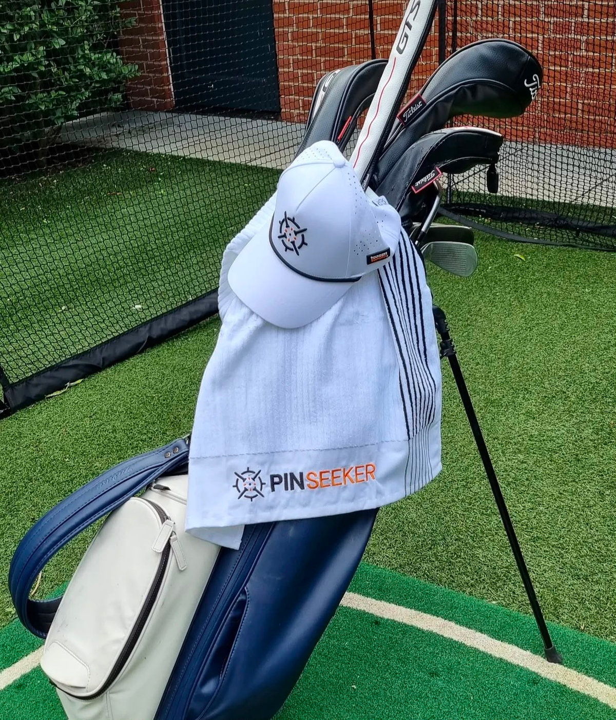 PINSEEKER Performance Golf Cap and golf towel in white, the Whiteout colourway, hanging on a golf bag