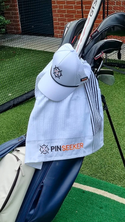 PINSEEKER Performance Golf Cap and golf towel in white, the Whiteout colourway, hanging on a golf bag