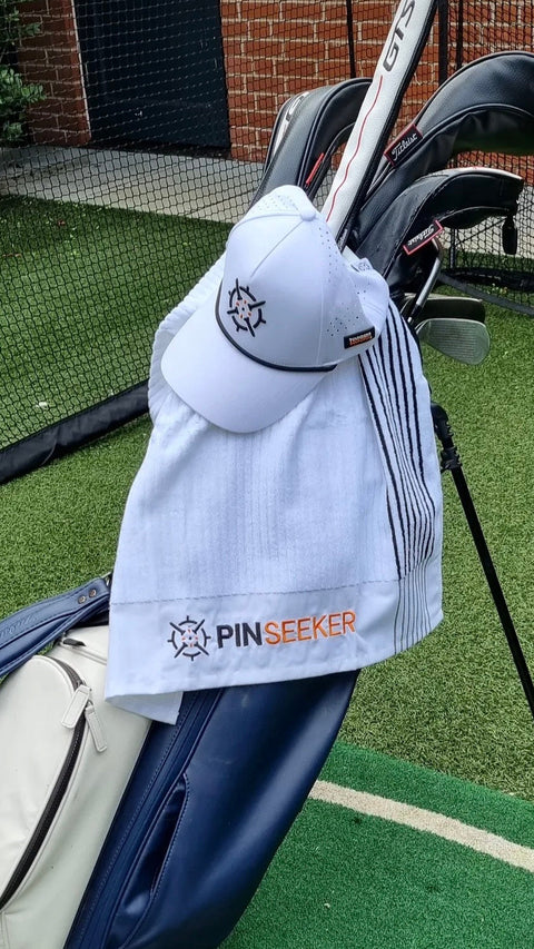 PINSEEKER Performance Golf Cap and golf towel in Whiteout, hanging on a golf bag